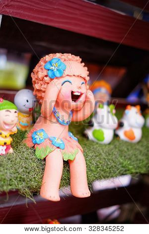 A Traditional Baked Cray Doll Of A Laughing Girl Sitting On A Shelf