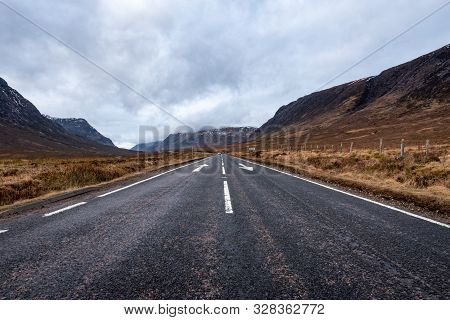 Road Going Towards Glencoe With Arrows, Lines And A Car In The Distance On A Cloudy Day In The Scott