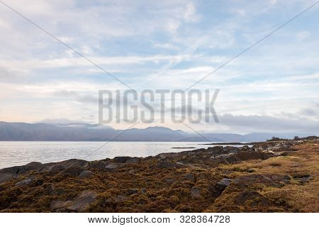 A Rocky Shoreline Covered In Seaweed Overlooking Loch Linnhe On A Partially Cloudy Day In The Scotti