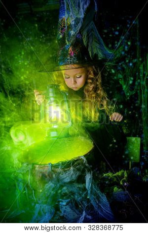 Happy Halloween. Cute child girl in witch costume is in a witch's lair. Cute cheerful little witch cooks a magic potion. 