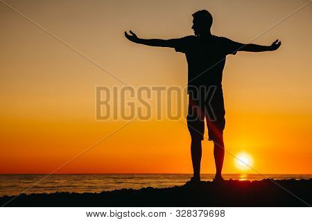 Silhouette Of A Man Stands And Contemplating On Beach On Sea Background And Sunset Flinging His Hand