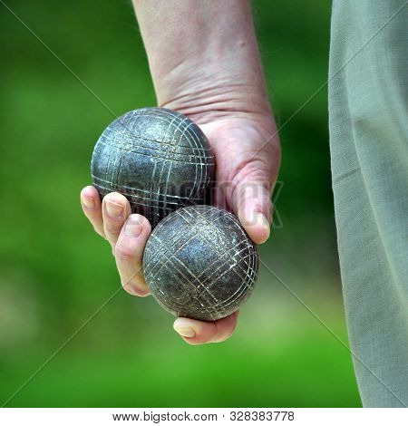Hand Holding Two Balls Of Petanque With A Green Background