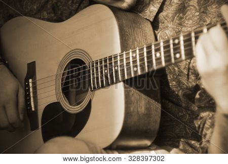 A Man In A Patterned Shirt Plays A Tune On An Acoustic Guitar, Illuminated By Sunlight And In A Sepi