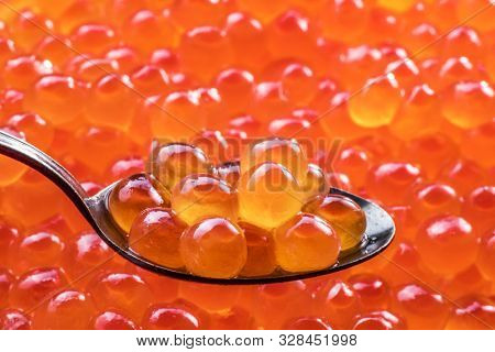 Salmon roe in the silver spoon close-up. Red caviar at the background.