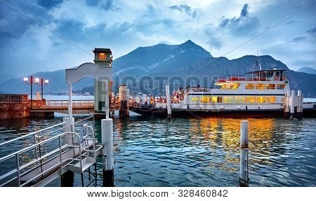 Bellagio village on lake Como, Italy. Ferryboat passenger transport by landing. Passengers ferry ship with arriving to the evening town. Evening time blue hour with dramatic sky and clouds.