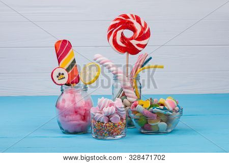 Sweet Candies In Glass Jars On Wooden Background. Colorful Candies, Jellies, Lollipops, Marshmallows
