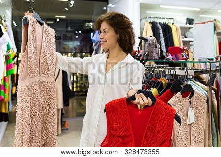 Attractive Young Woman Chooses Dress For A Date Standing Among Garment Racks With Pale Pink Dress In