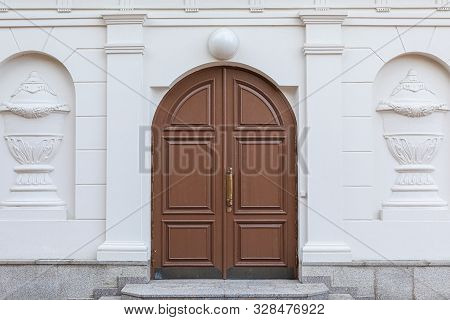 Double Brown Wooden Arched Vintage Door With Lamp Above It In White Wall With Bas-relief And Granite