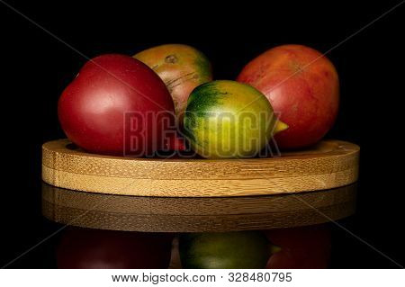 Group Of Four Whole Fresh Tomato De Barao On Round Bamboo Coaster Isolated On Black Glass