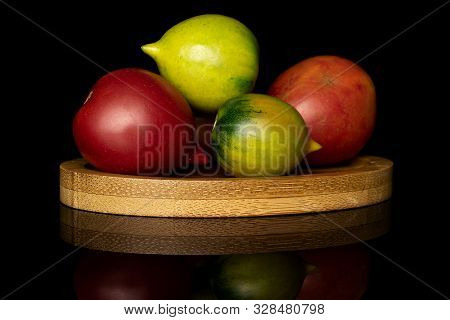 Group Of Five Whole Fresh Tomato De Barao On Round Bamboo Coaster Isolated On Black Glass