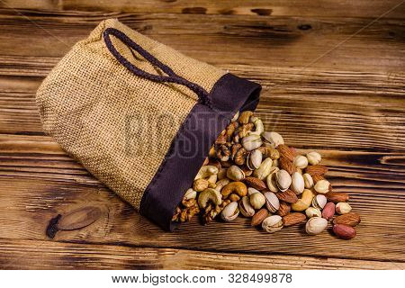 Various Nuts (almond, Cashew, Hazelnut, Pistachio, Walnut) Scattered From Bag On Wooden Table. Veget