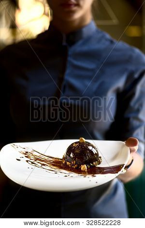French Mini Mousse Pastry Dessert In Chocolate Icing On A Plate. Dessert In The Hands Of A Waitress.