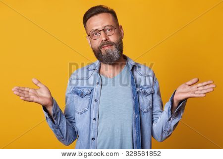 Handsome Middle Aged Man With Beard And Stylish Hairdo Spreads Hands, Does Not Know What To Answer, 