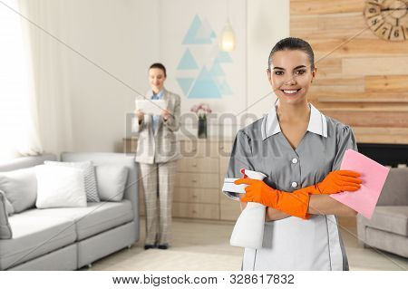 Portrait Of Young Chambermaid And Blurred Supervisor In Hotel Room. Space For Text