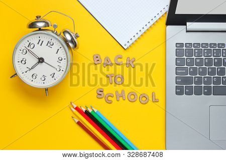 Scholl Time Minimalistic Concept. Laptop, Color Pencils, Notebook, Alarm Clock On Yellow Background.