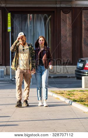 Couple Walking Holding Their Hands On The Sidewalk Of Victoriei Way (calea Victoriei) In Bucharest,