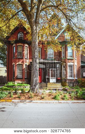 Red Brick Houses And Mansard Roofs With Garden And Tree In Autumn. Gananoque, Canada.