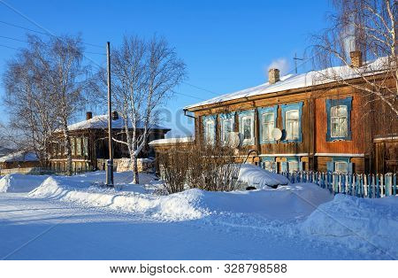 Snow-covered Village Street In Winter. View Of The Old Residential Neighborhood On A Sunny Winter Da