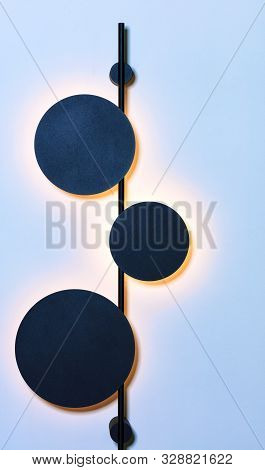 Stylish Vertical Metal Wall Lamp In The Form Of Three Celestial Bodies In An Eclipse Against A Blue 
