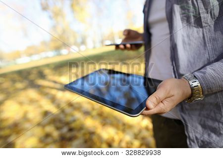 Man In Pakr Hold Digital Tablet Pc In Park Against Yellow Leaves Background Closeup. Autumn Sales Co