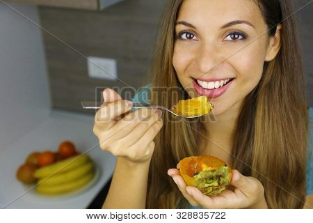 Beautiful Young Woman Smiling And Eating Persimmon Kaki Fruit At Home. Close Up From Above. Healthy 