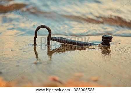 An Old Rusty Lost Treasure Key, Lying In The Sand In The Surf On The Beach. The Concept Of Luck And