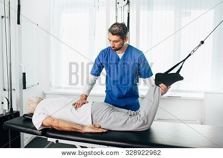 Kinesiologist Doing Therapeutic Exercises For An Elderly Patient. Kinesitherapy At The Medical Cente