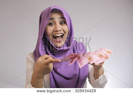 Portrait Of Indonesian Muslim Woman Holding Rupiah Money, Smiling Laughing Winning Gesture
