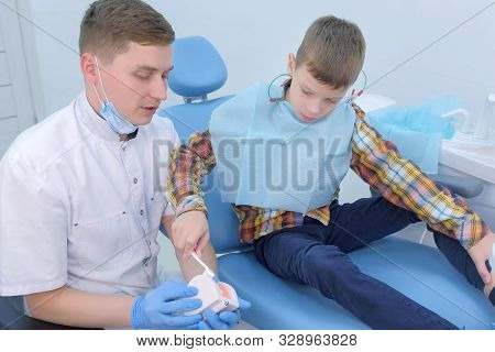 Dentist Teaching Patient Child Boy How To Clean Teeth Using Toy Jaw Model. Showing Massaging Movemen