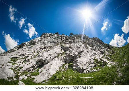 Hikers Walking On Trail. Group Of People Hiking In Mountains With Blooming Meadows And Mountain Peak