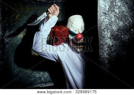 Scary Clown, In The Shadows, Looking Eerily At The Camera From Behind An Abstract Wall. Halloween Co