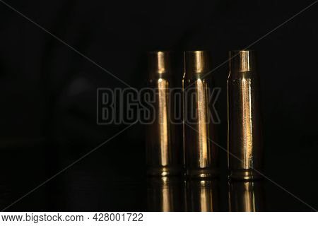 Spent Cartridges On A Black Background. Three Empty Cartridge Cases Are Lined Up Side By Side. Close