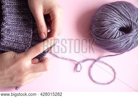 Female Hands With Knitting Needles To Knit Wool Violet Sweater And Tangle Of Woolen Thread On Pink B