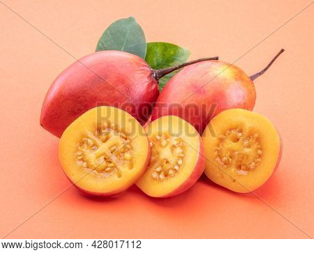 Ripe tamarillo fruits with slices and tamarillo leaves isolated on a orange background.