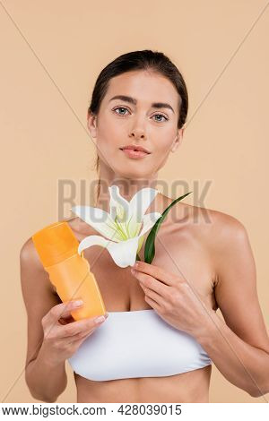Pretty Woman With Sunscreen And White Lily Looking At Camera Isolated On Beige