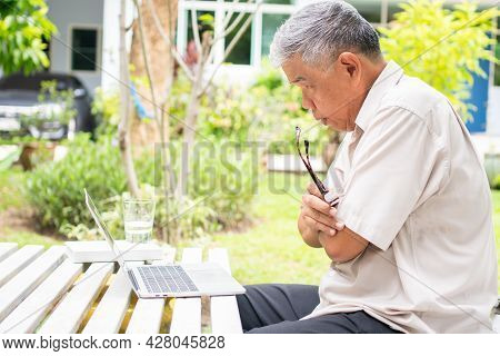 Portrait Of Old Elderly Asian Man Using A Computer Laptop In The Backyard For Learning New Skill Aft