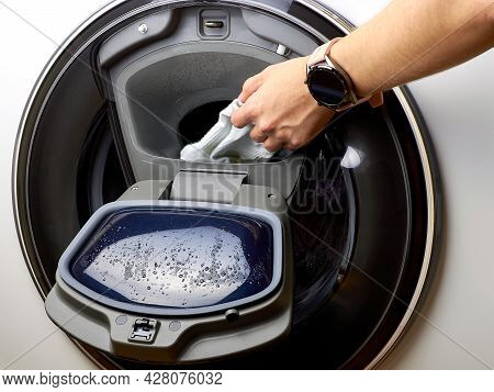 Function Adding Laundry During Washing. A Person Puts Clothes In The Washing Machine. House Cleaning