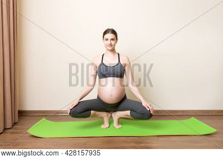 Beautiful Young Pregnant Woman Sitting On Mat In Yoga Pose At The Home. Pregnancy Yoga And Fitness C