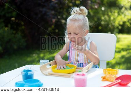Little Cute Girl With Blonde Hair Playing With Kinetic Sand Outdoors In The Backyard In Summer Day