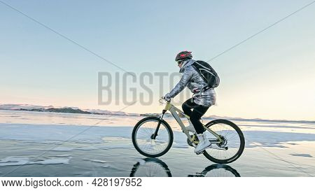 Woman Is Riding Bicycle On The Ice. Tires On Bike Are Covered Wi