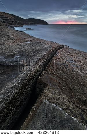 A Close Up Of A Rock Next To A Body Of Water At Sunrise