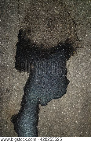 A Puddle And Wet Spots On The Asphalt In The Form Of The Head Of A Black Man With A Large Light Hair