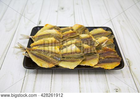 Yellow Tabby (latin: Selaroides Leptolepis) Dried Folded In Rows On A Black Rectangular Plate With A