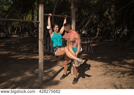 Trainer Helping A Fit Young Woman To Do Pull-up Her Arms On The Park. Sport Actuvity To Stay Healthy
