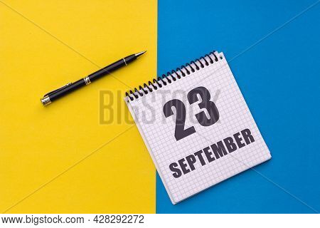 September 23th. Day 23 Of Month, Calendar Date. Notebook With A Spiral And Pen Lies On A Yellow-blue