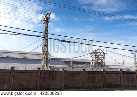 Long Dark Wall Separating A Large Industrial Facility From The Street, Heavy Electrical Power Lines 