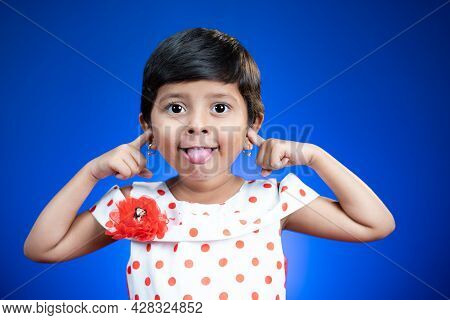 Litte Girl Kid With Tongue Out Or Grimacing Dancing On Blue Background - Happy, Cheerful And Crazy K