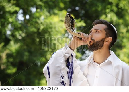 Jewish Man In Kippah And Tallit Blowing Shofar Outdoors. Rosh Hashanah Celebration