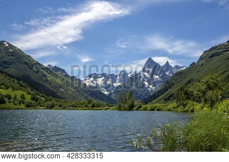 Landscape With A Mountain Lake On A Summer Day. Blue Sky With Clouds. Grass In The Foreground. Mount
