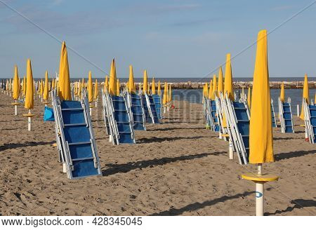 Many Yellow Closed Umbrellas And Sun Loungers On The Deserted Beach Without People